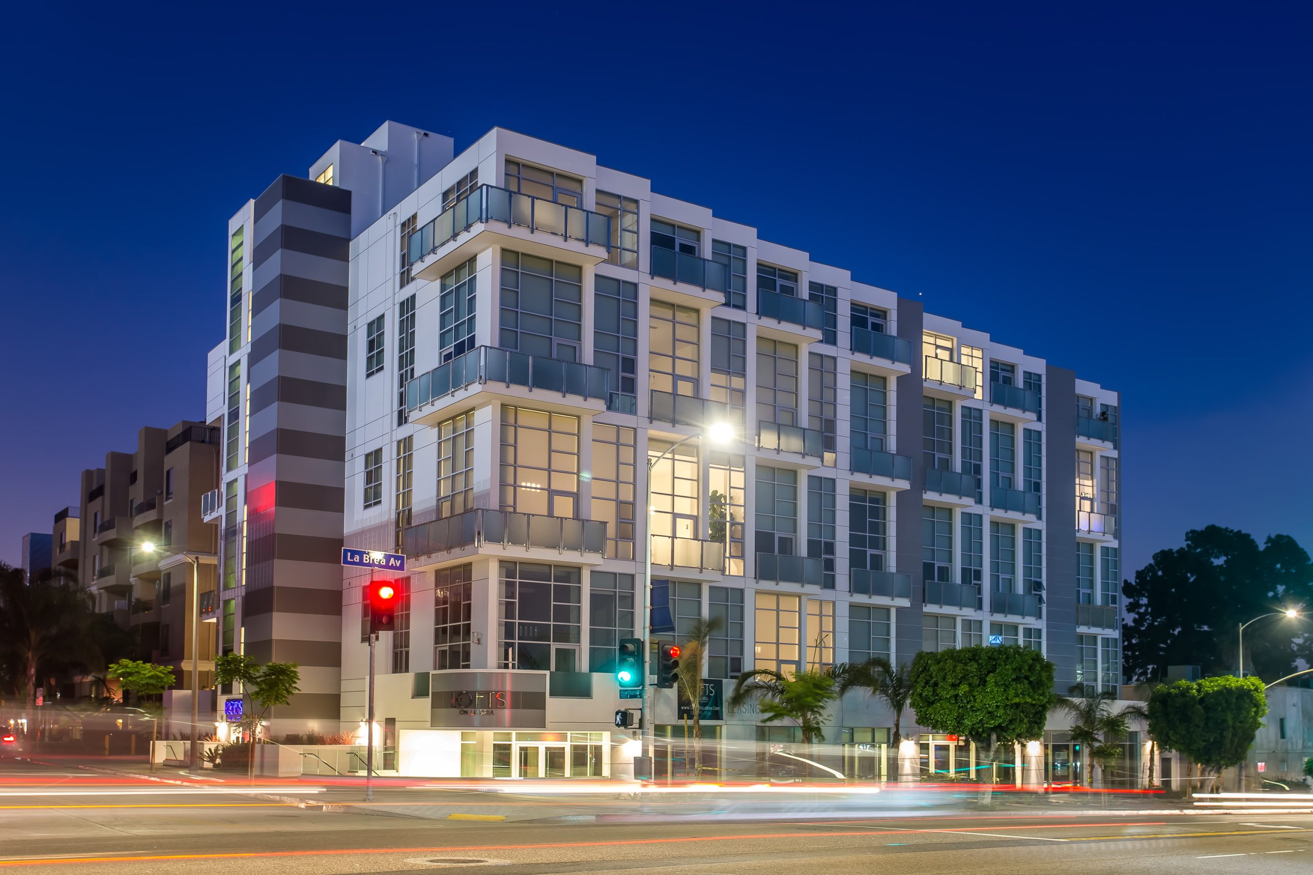 Modern mixed-use apartment building illuminated at night on city street corner.