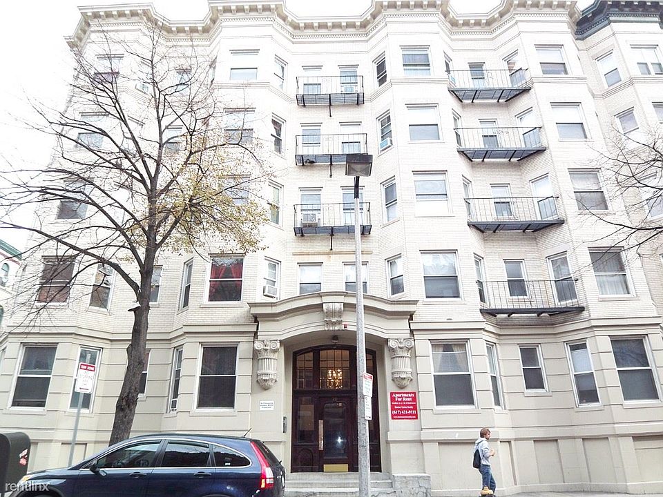 Historic apartment building with a white stone façade, decorative architectural details, and private balconies along a tree-lined city street.