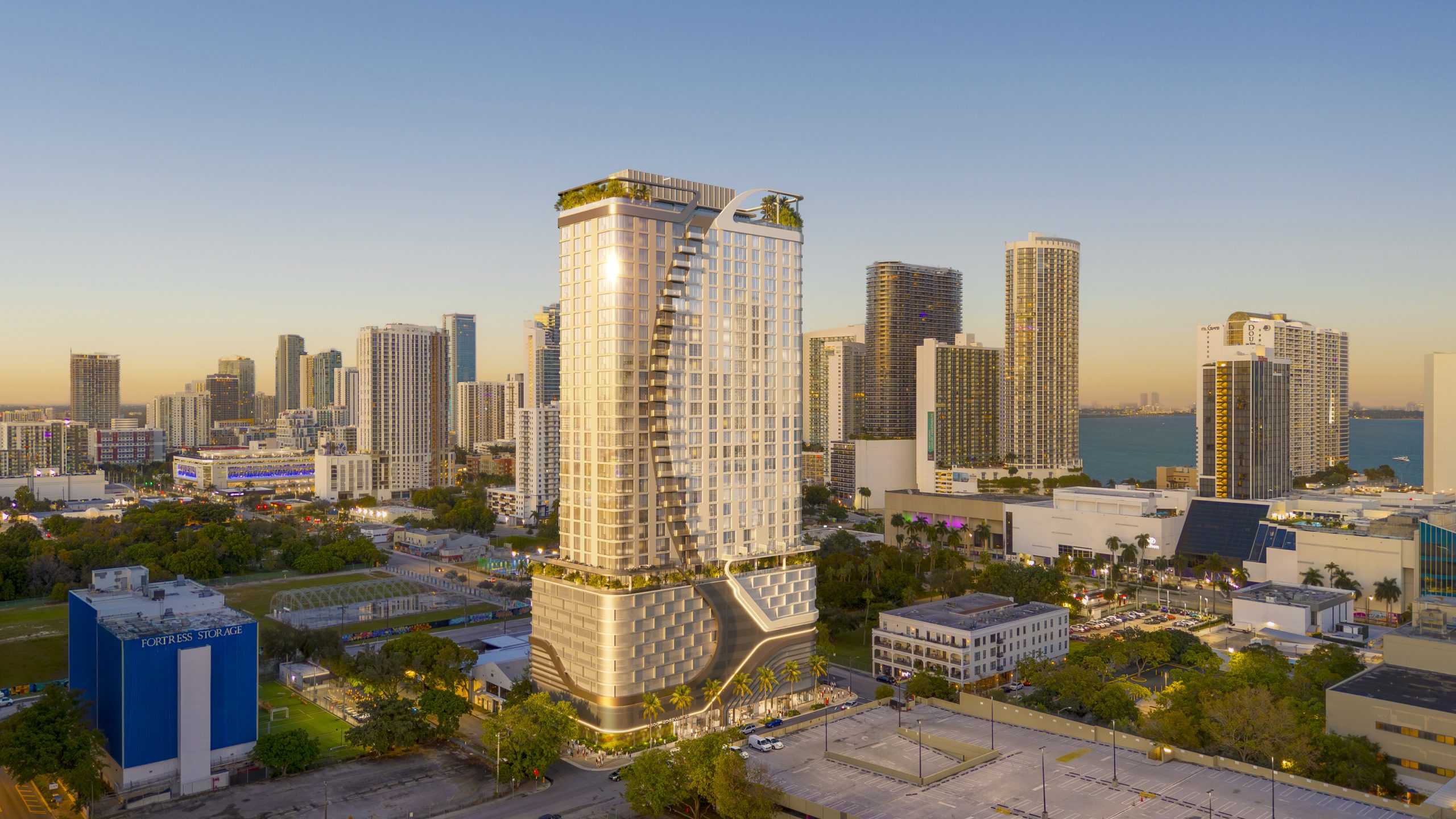 Modern high-rise residential tower rising above a city skyline, surrounded by urban buildings and green spaces.