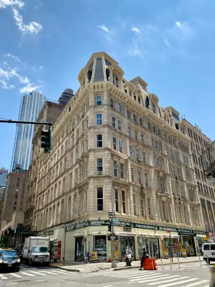 Elegant historic corner building with ground-floor retail space, detailed masonry façade, and surrounding city streetscape under a clear blue sky.