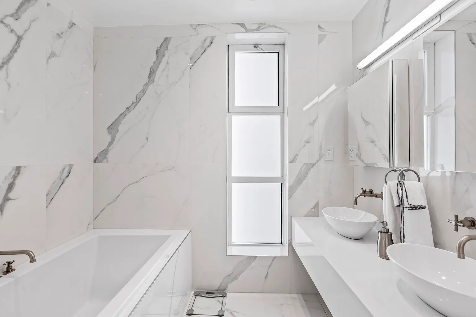 Elegant bathroom with marble-look wall finishes, a soaking tub, glass shower enclosure, and contemporary fixtures.