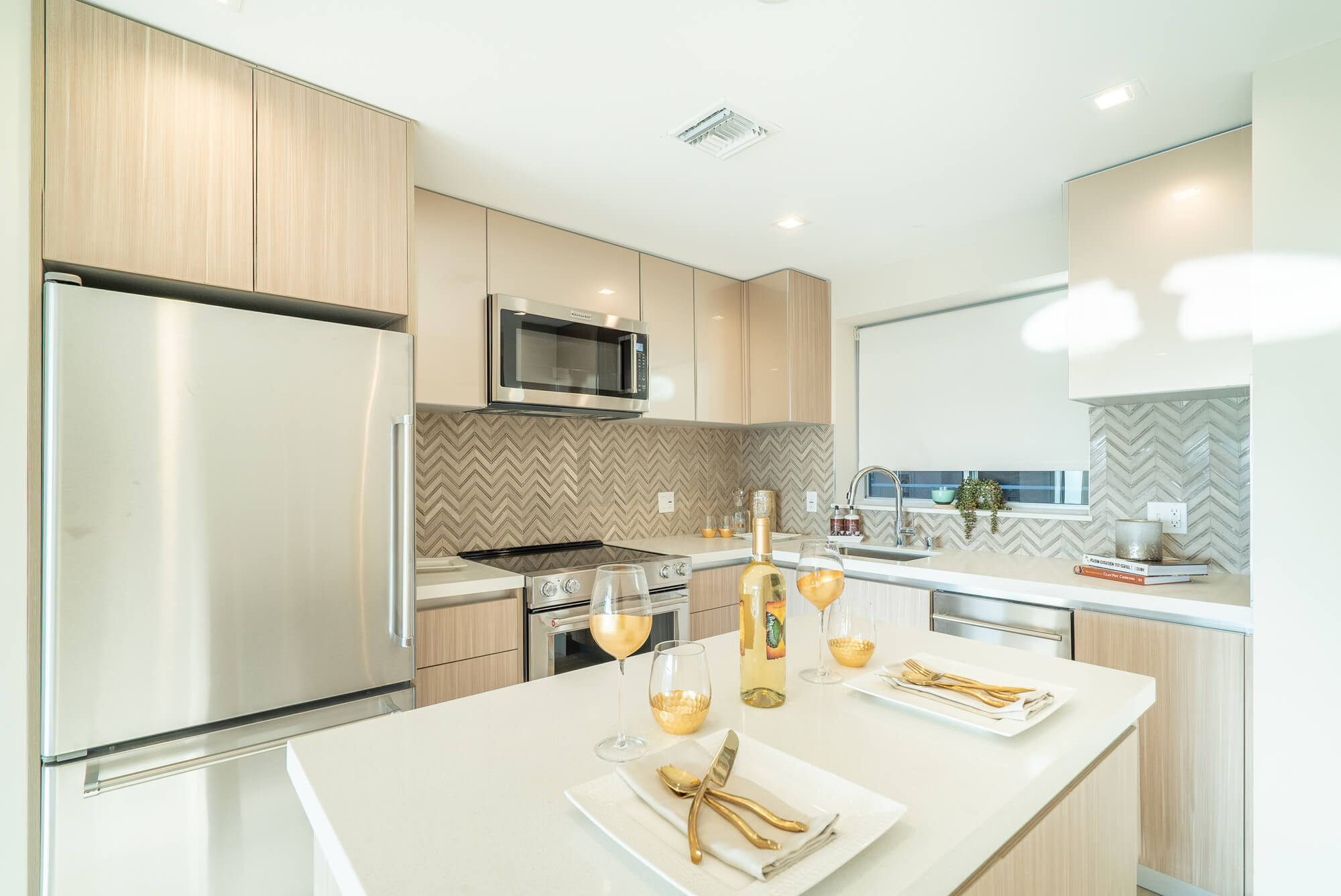 Modern apartment kitchen featuring light wood cabinetry, stainless steel appliances, and a center island.