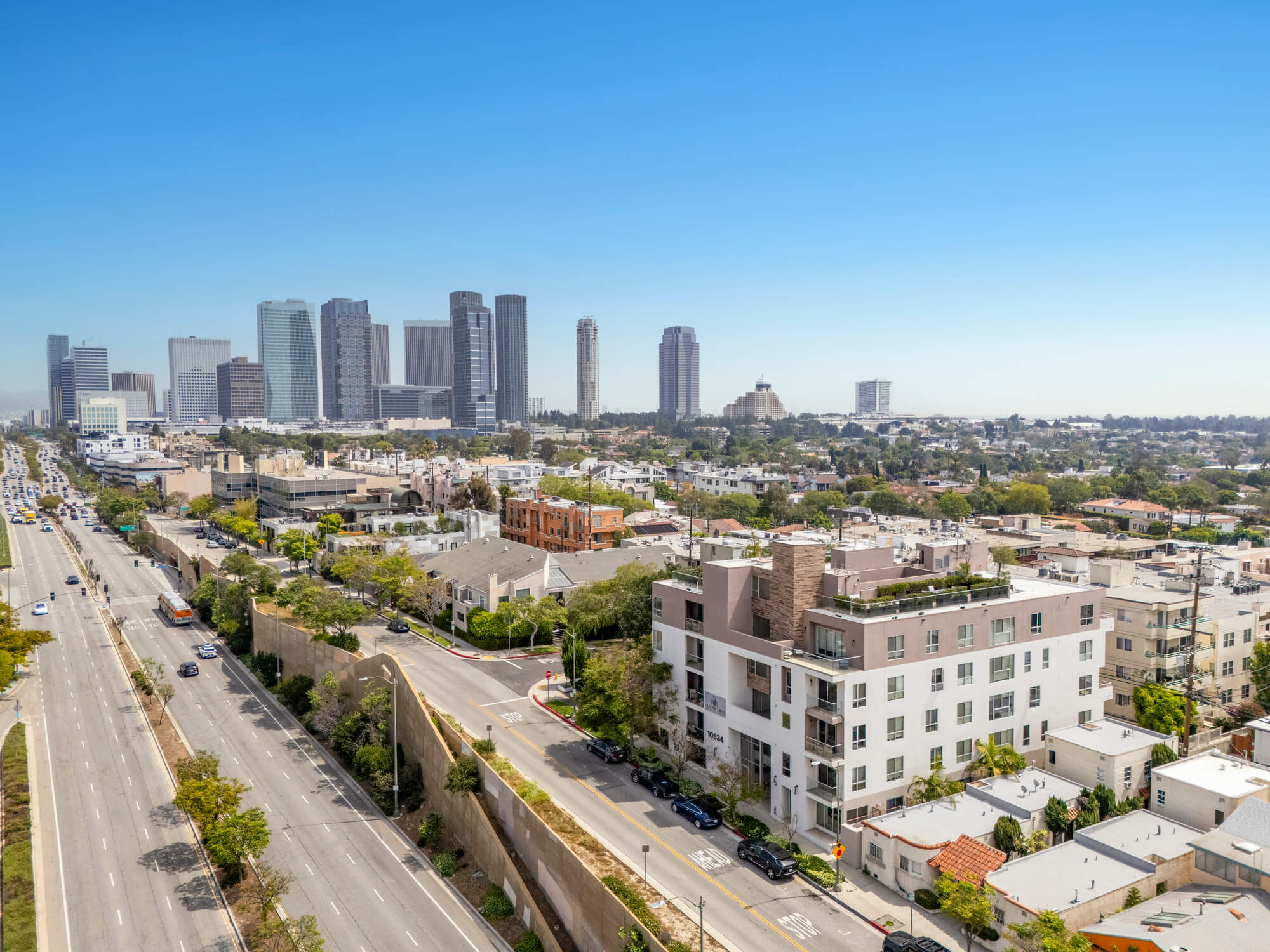 Aerial view of a mixed-use urban neighborhood with residential buildings, major roadways, and a downtown skyline in the distance.