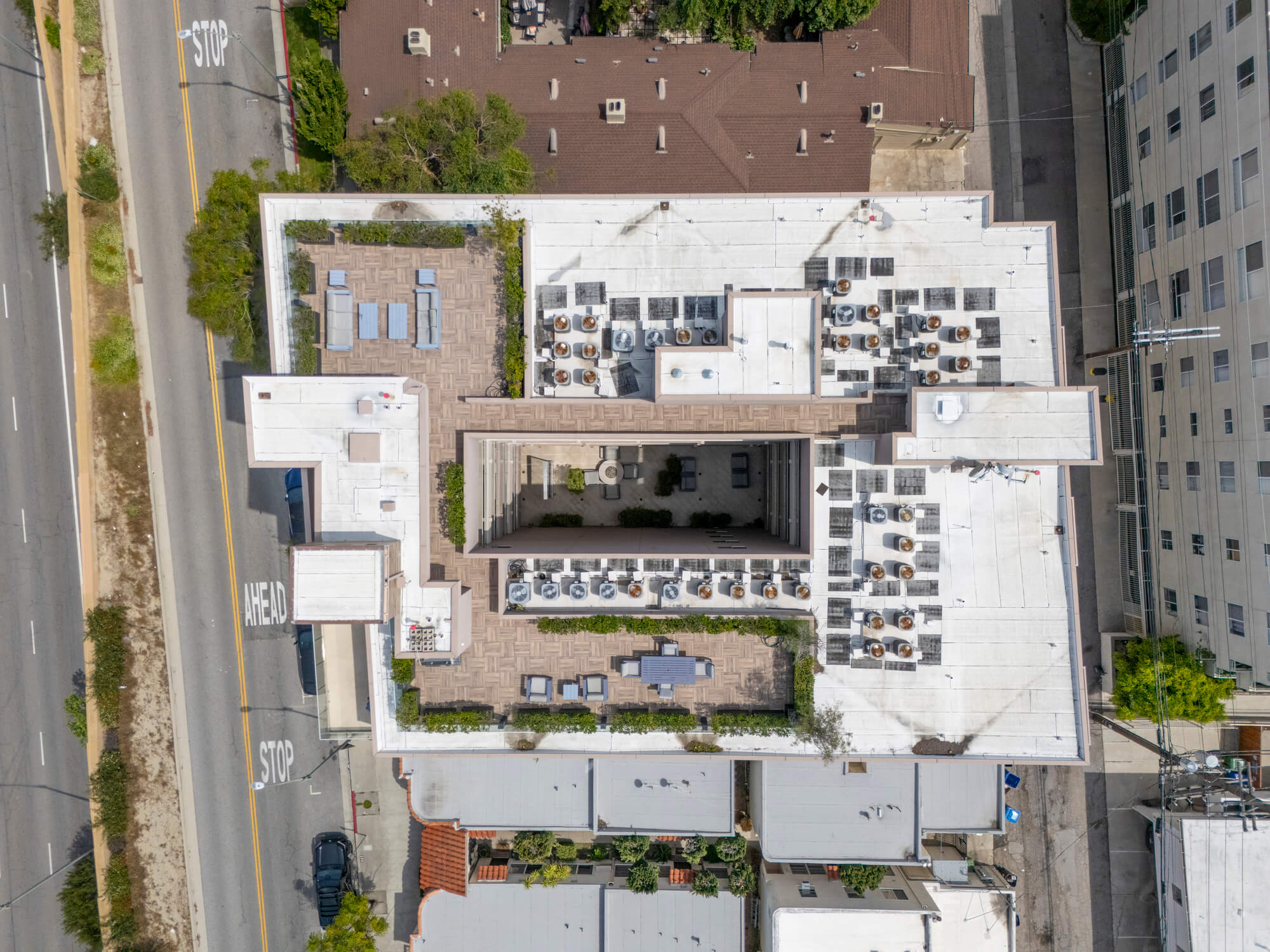 Top-down drone view of a multifamily residential development showcasing building layout, rooftop amenities, and surrounding streets.