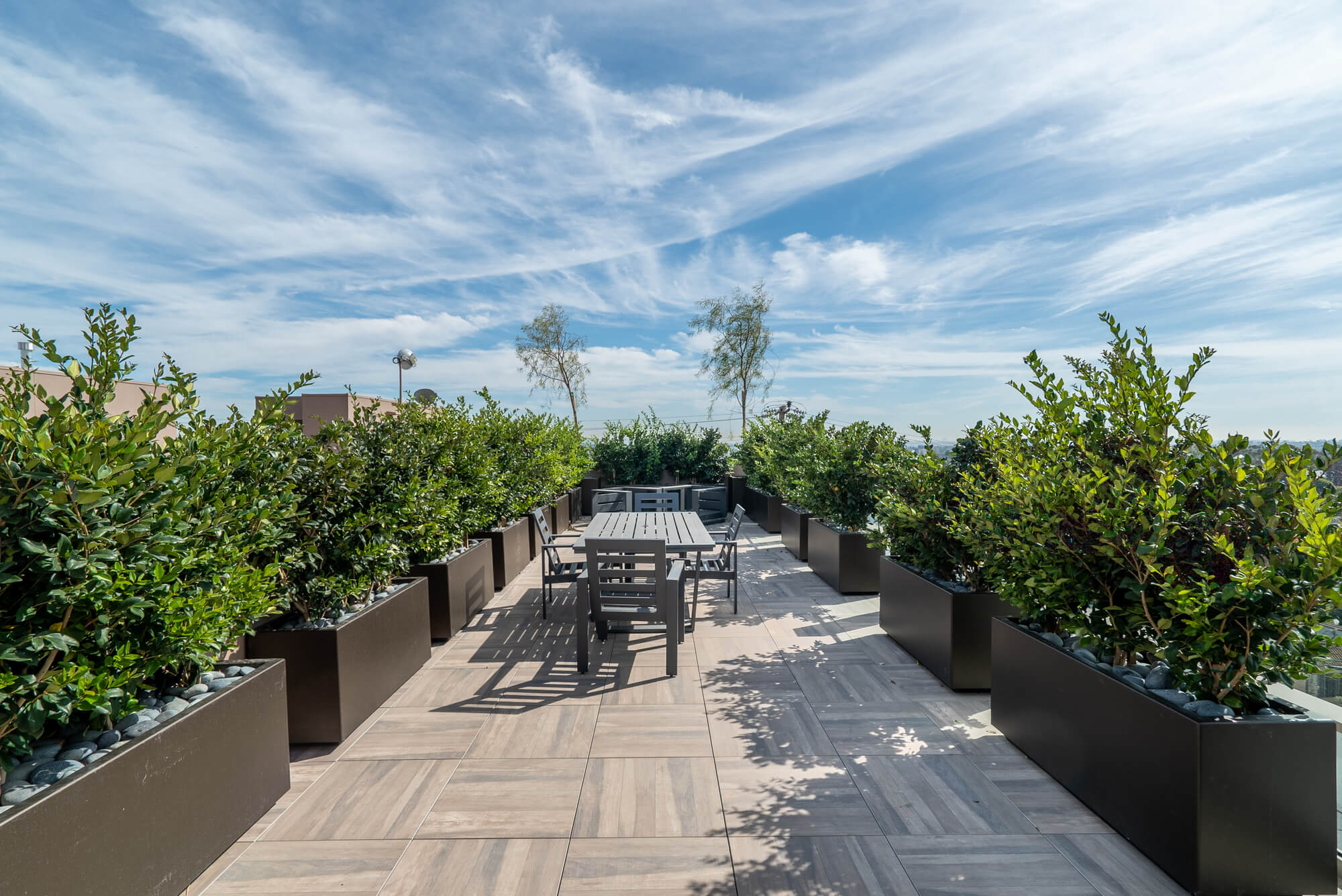 Landscaped rooftop terrace with outdoor seating, walking areas, and expansive views under a clear sky.