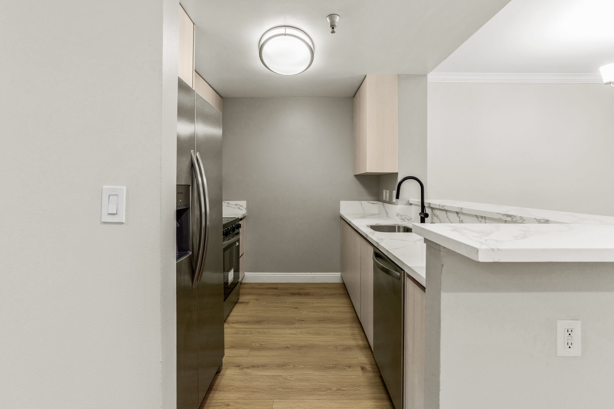 Contemporary galley-style kitchen featuring stone countertops, stainless steel appliances, and light wood cabinetry.