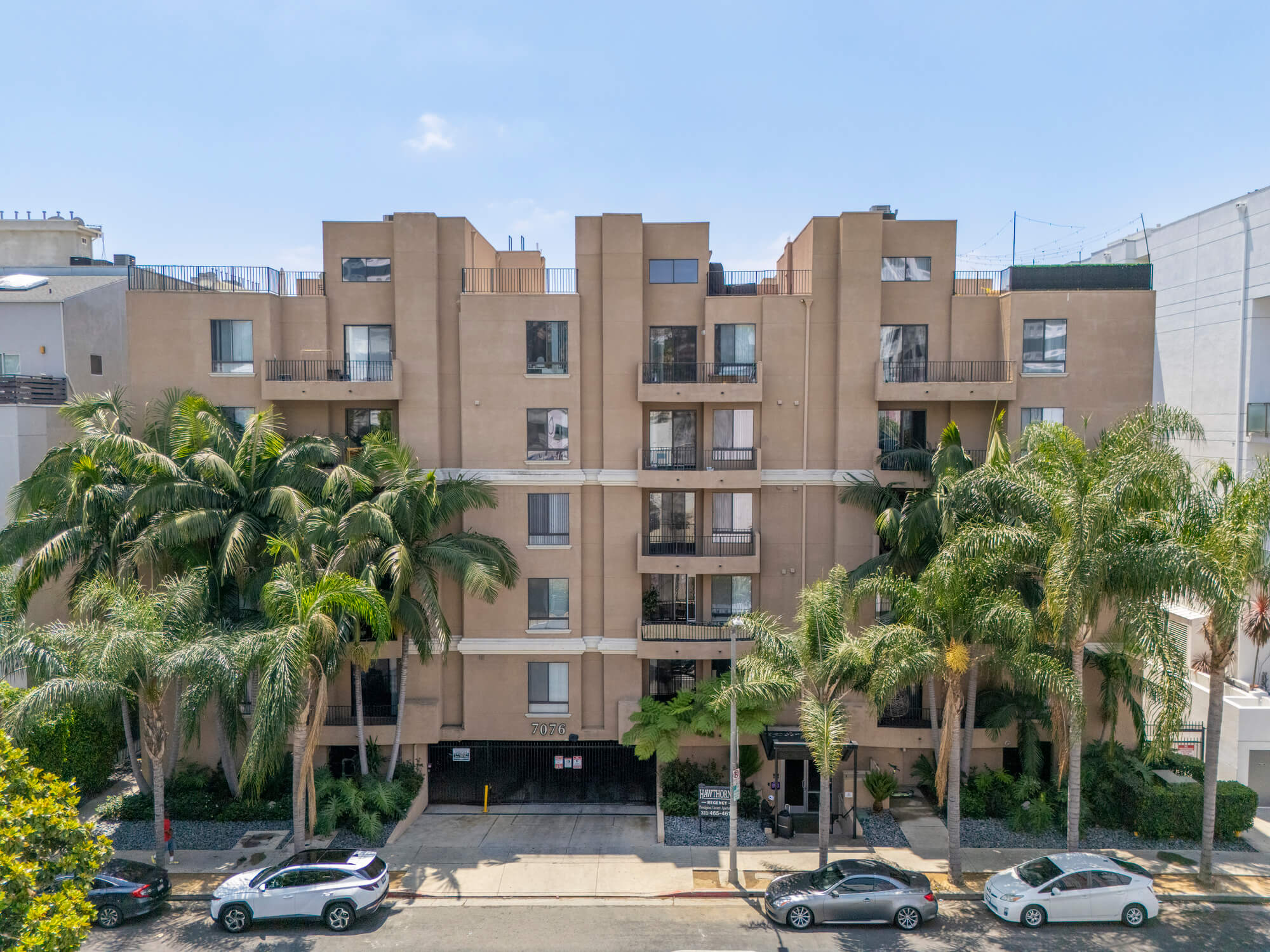 Mid-rise apartment building surrounded by mature palm trees and landscaped grounds in an urban residential neighborhood.