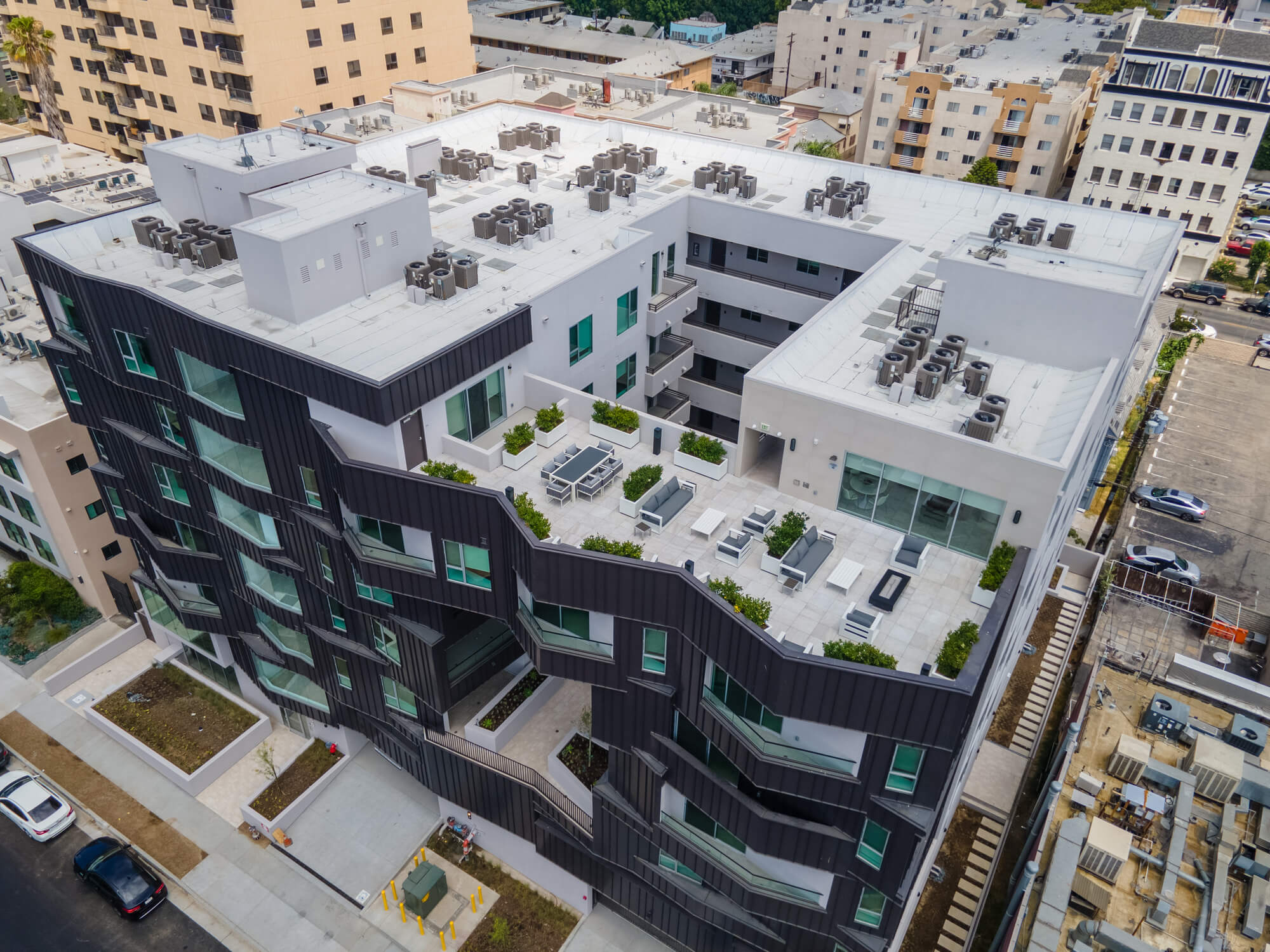 Drone view of a modern multifamily residential development showcasing rooftop amenities and surrounding city streets.