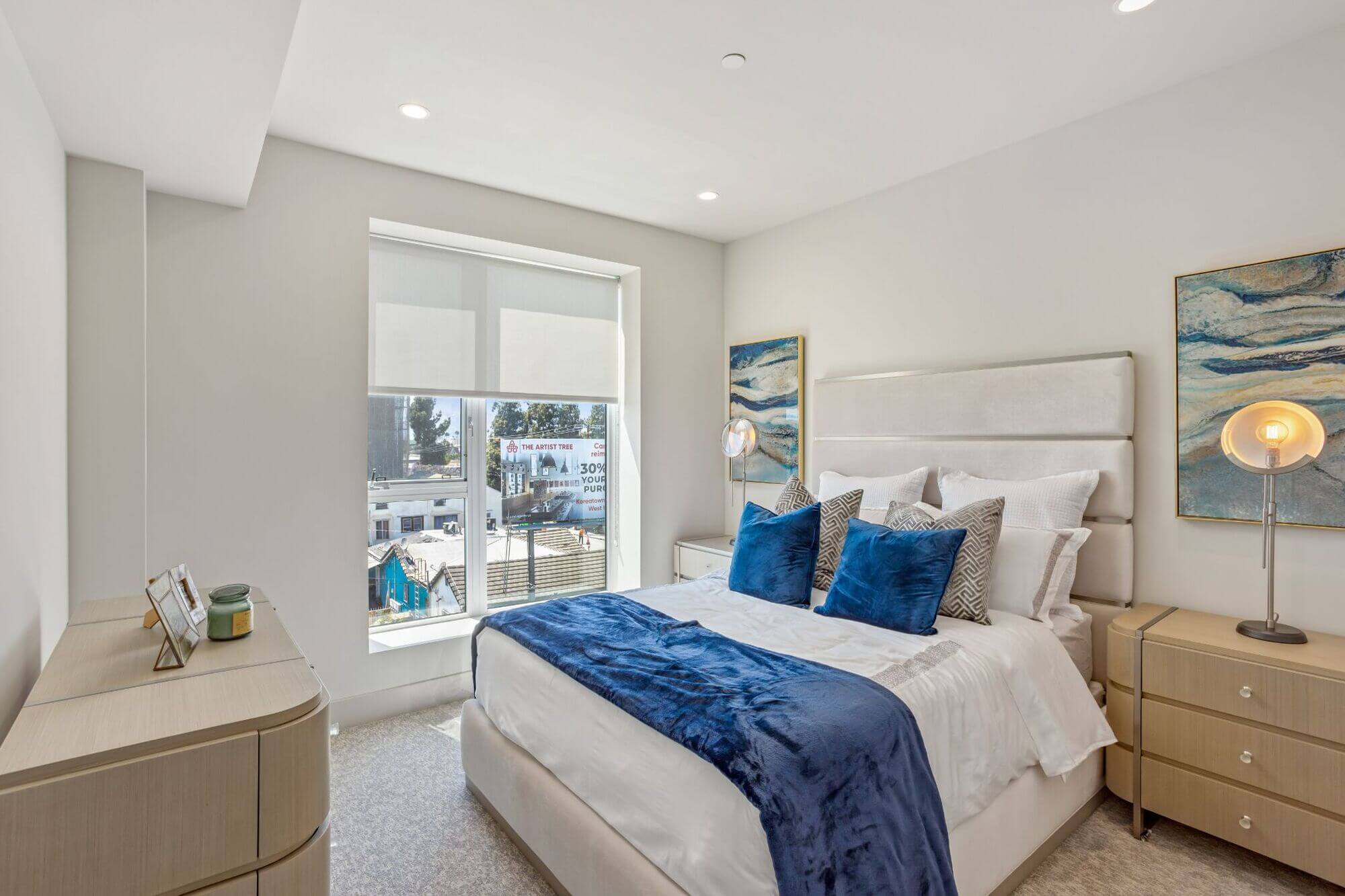 Bright apartment bedroom featuring large windows, modern furnishings, and neutral finishes.