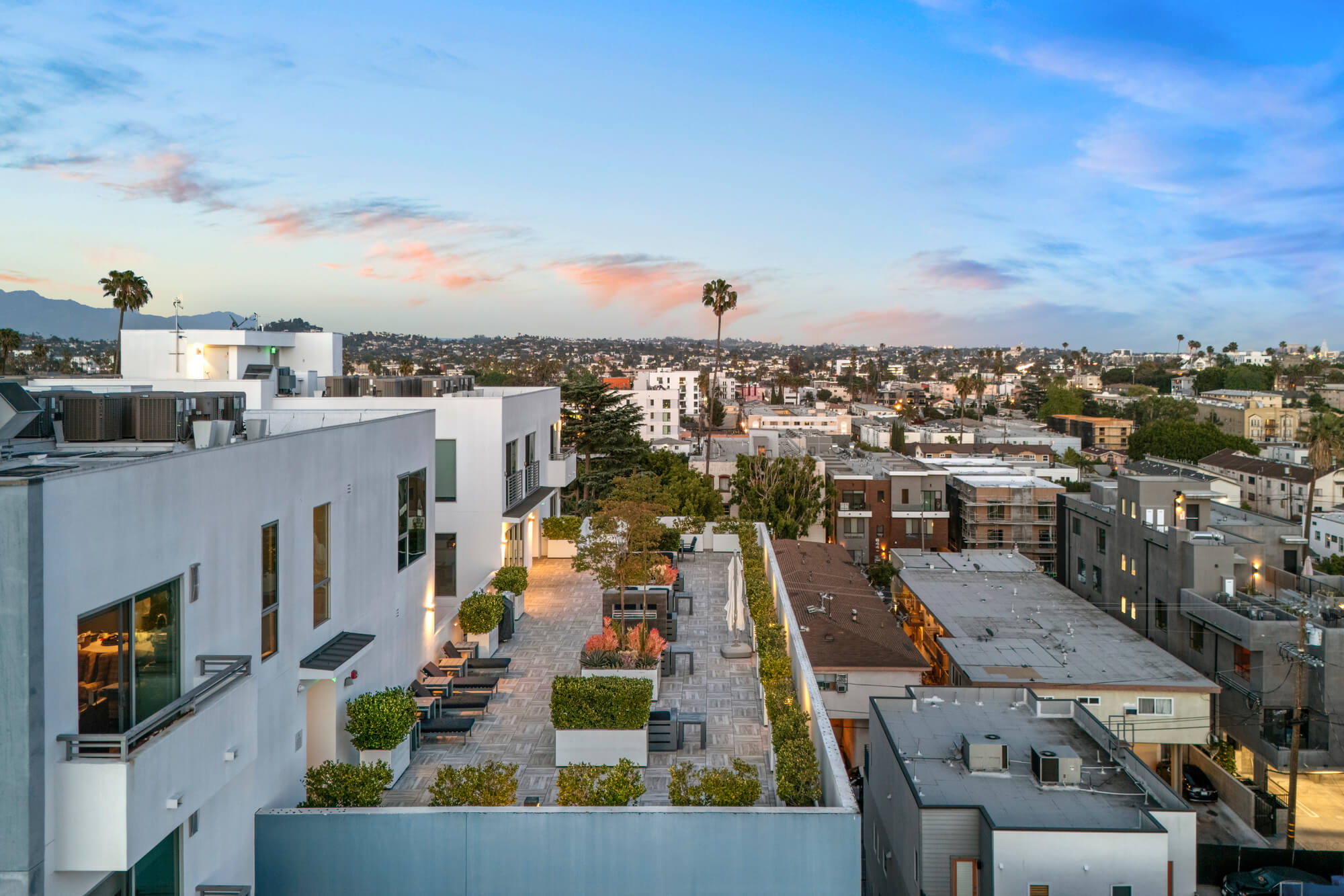 Elevated view of a mixed-use residential development with landscaped walkways and surrounding urban neighborhoods at sunset.
