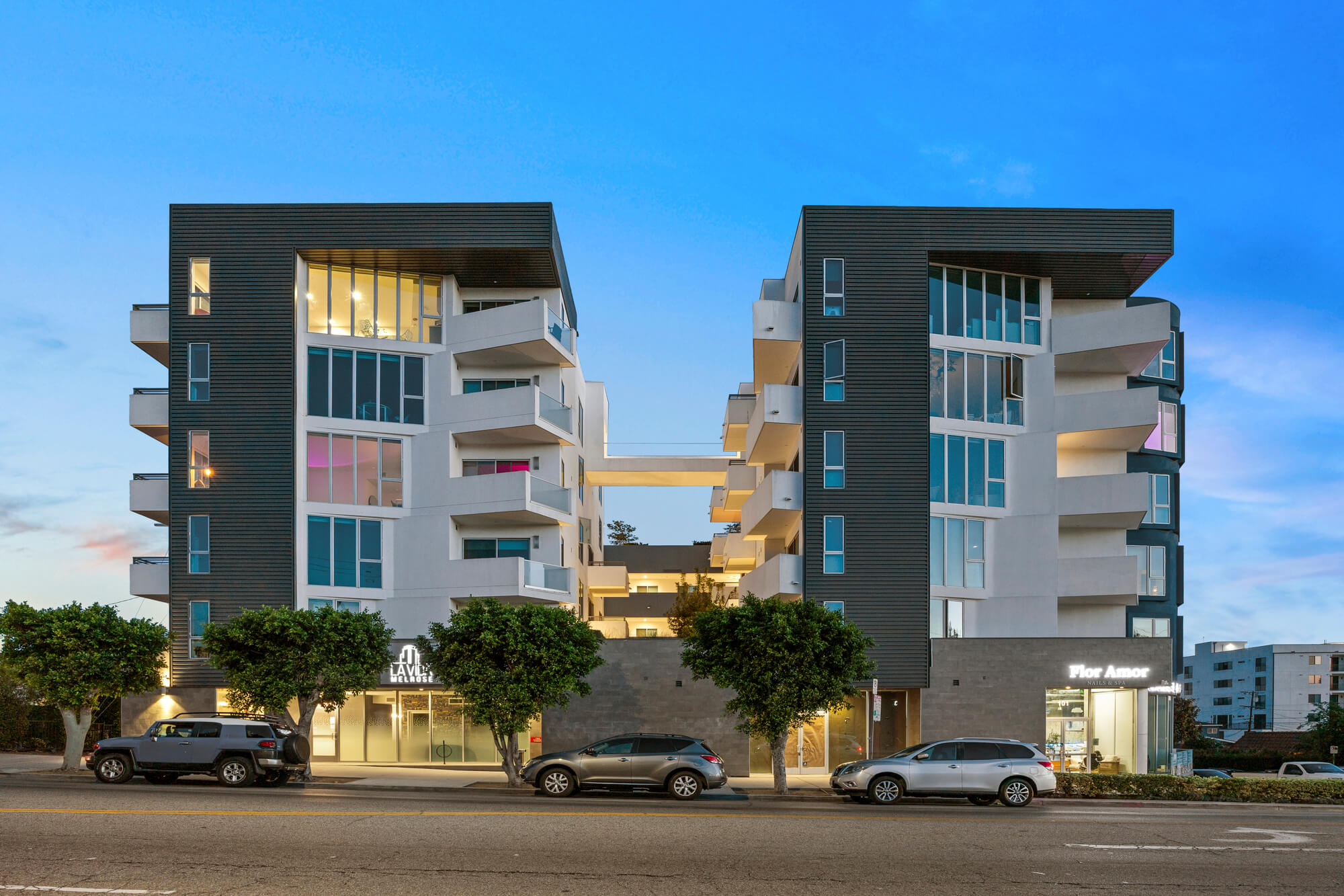 Contemporary multifamily residential building with modern architecture, balconies, and street-level landscaping.