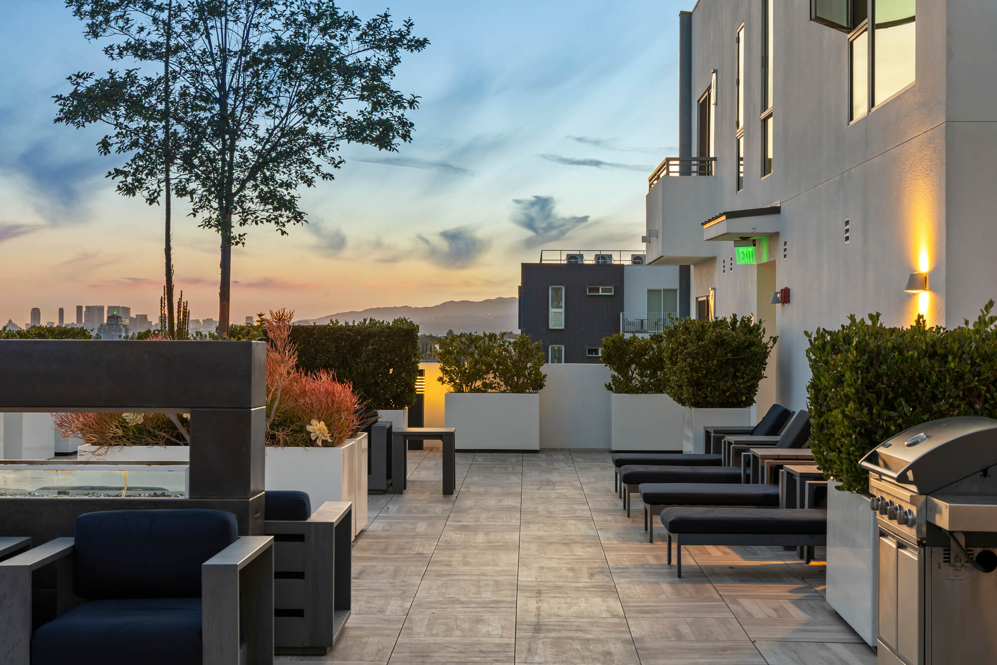 Luxury rooftop terrace with lounge seating, landscaped planters, and outdoor gathering spaces at sunset.