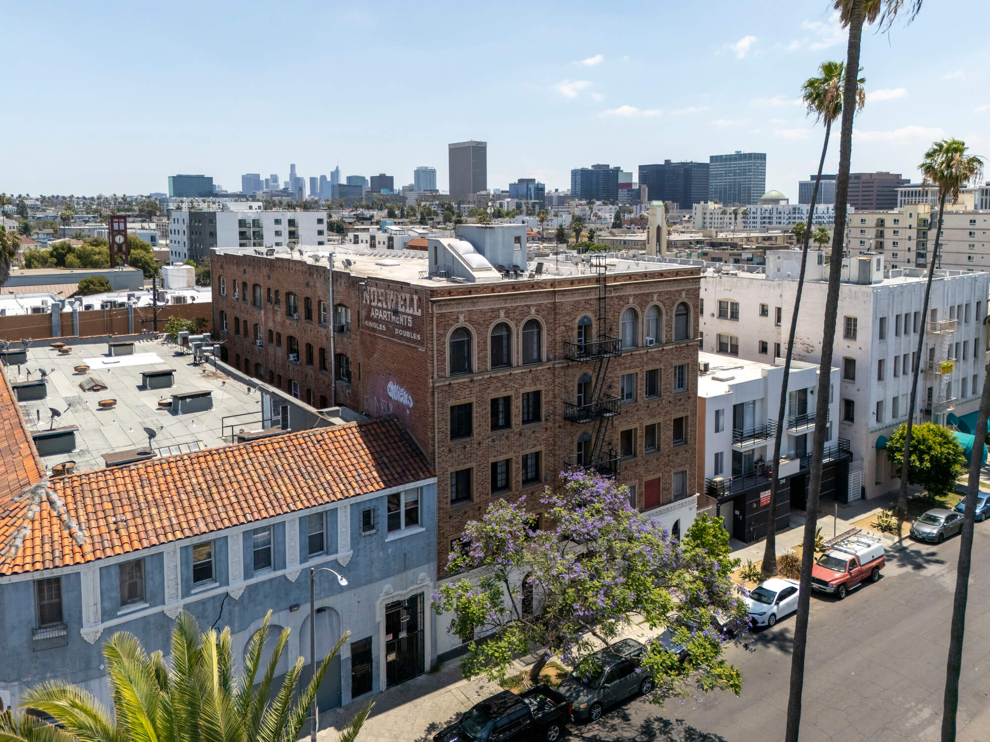Elevated view of a multifamily residential property overlooking neighboring buildings, palm trees, and a walkable urban streetscape.