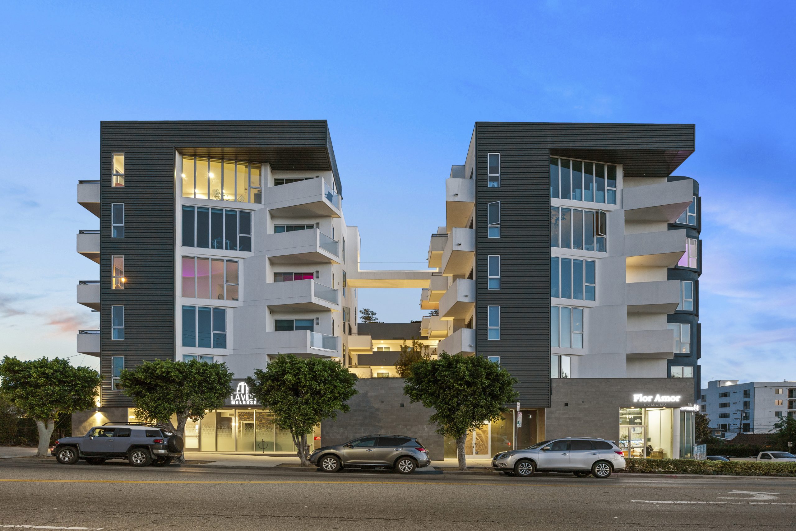 Modern mid-rise apartment building with balconies, contemporary architecture, and landscaped frontage along a city street.