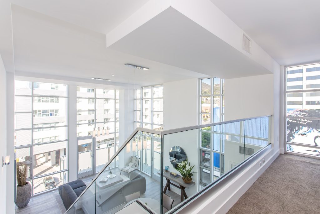 Bright modern apartment interior with open loft layout and glass staircase railing.