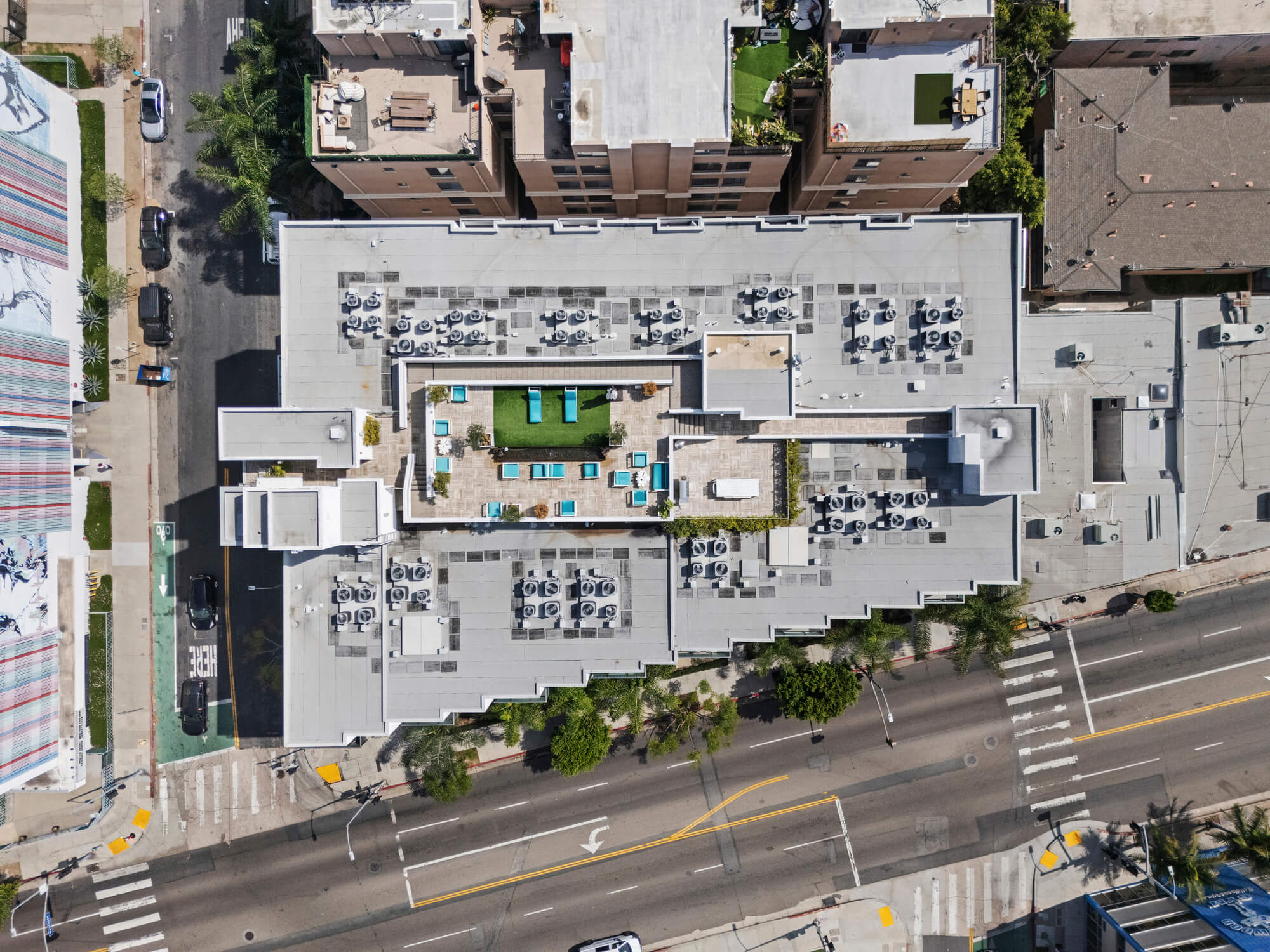 Top-down aerial view of a multifamily development showcasing rooftop amenities, building layout, and surrounding streets.