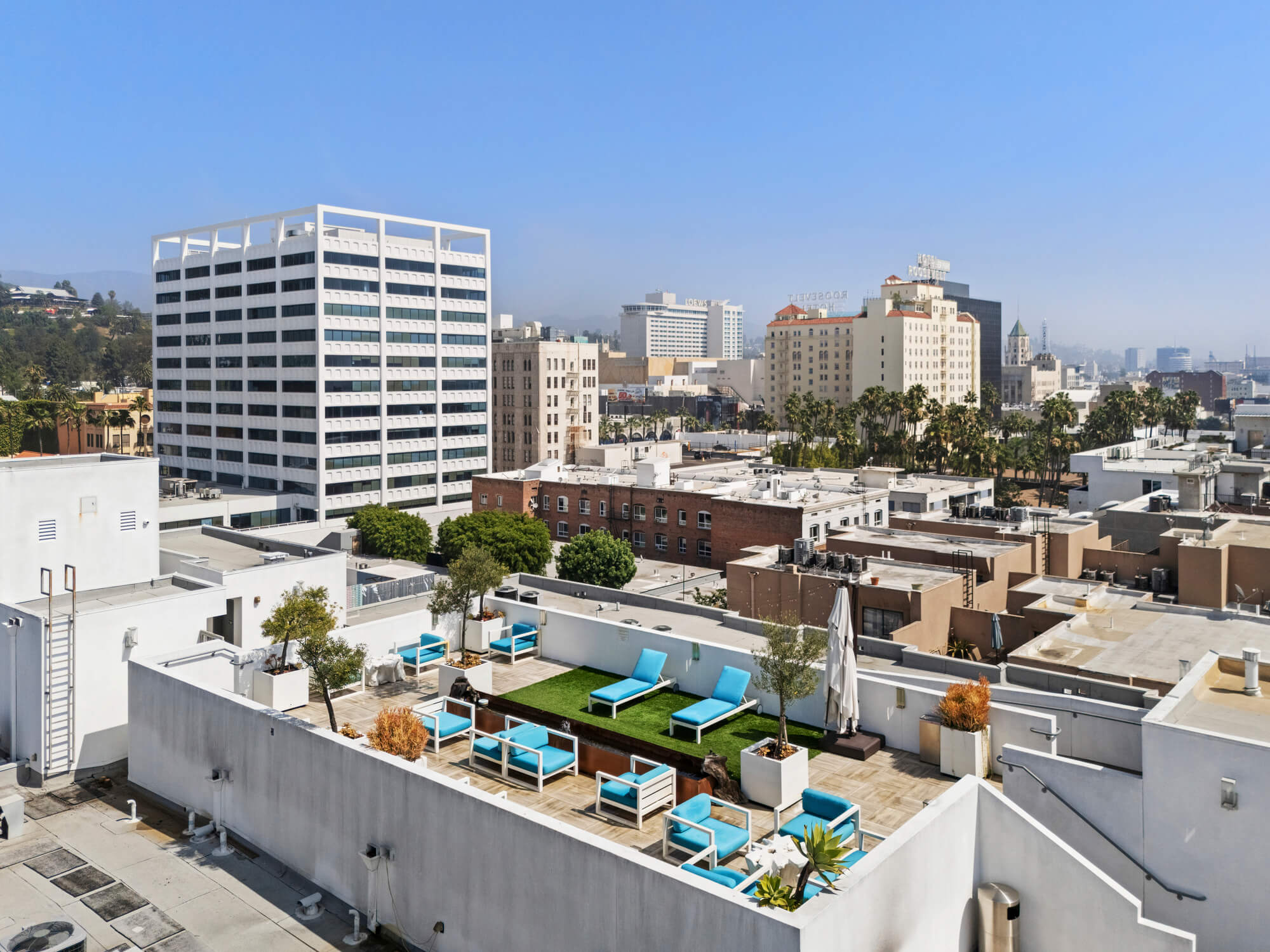 Elevated view of a rooftop amenity deck with lounge seating, landscaping, and surrounding city buildings.