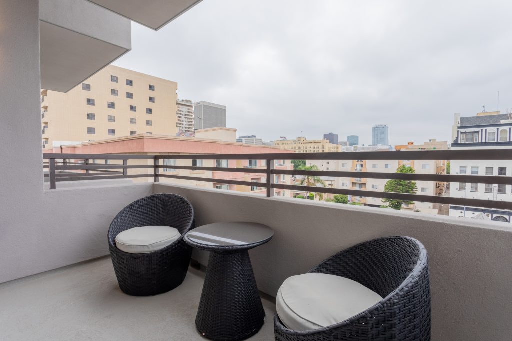 Modern apartment balcony with outdoor chairs and urban skyline backdrop.