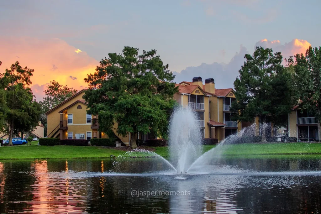 Residential community pond with fountain and sunset reflections near apartment homes.
