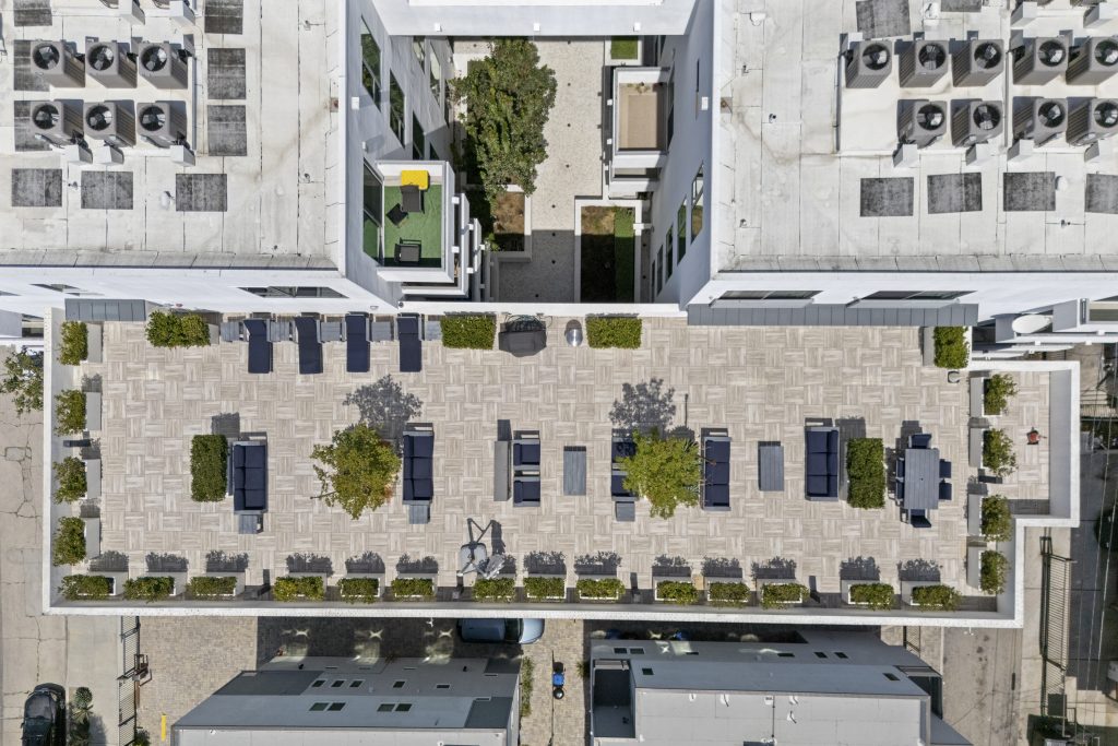 Aerial top-down view of modern mixed-use real estate development with parking and rooftop spaces.